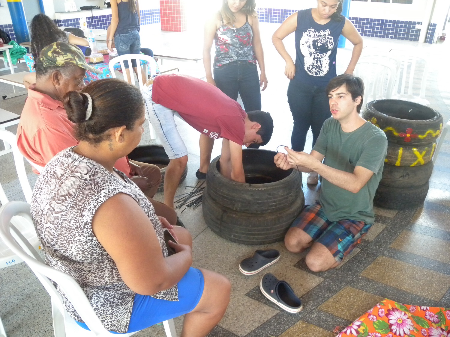O estudante de odontologia, Romero Albuquerque, explica à dona Eliene e ao seu José Dionísio como usar a abraçadeira de nylon na montagem da lixeira com pneus usados(Foto: Ascom UFS Lagarto)